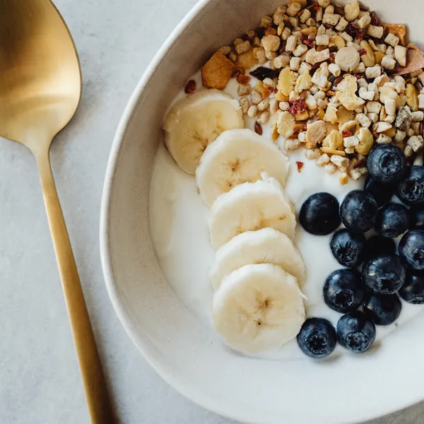 A bowl of yogurt topped with banana slices, chopped nuts and blueberries