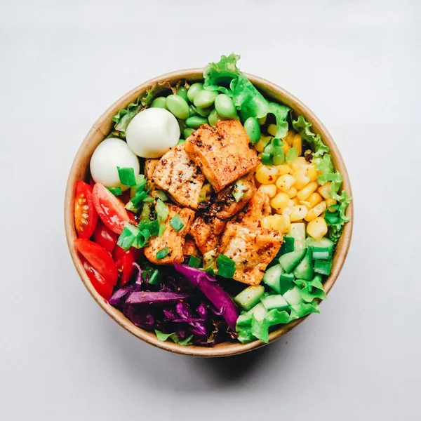 A bowl of chicken, egg, greens, corn and red cabbage