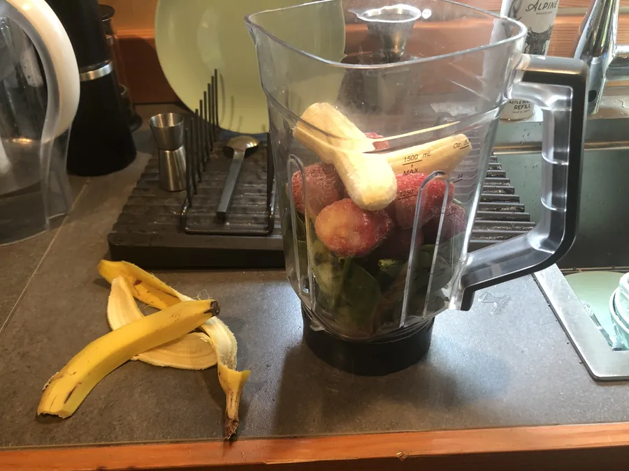 A blender filled with spinach, berries and banana on a home kitchen counter