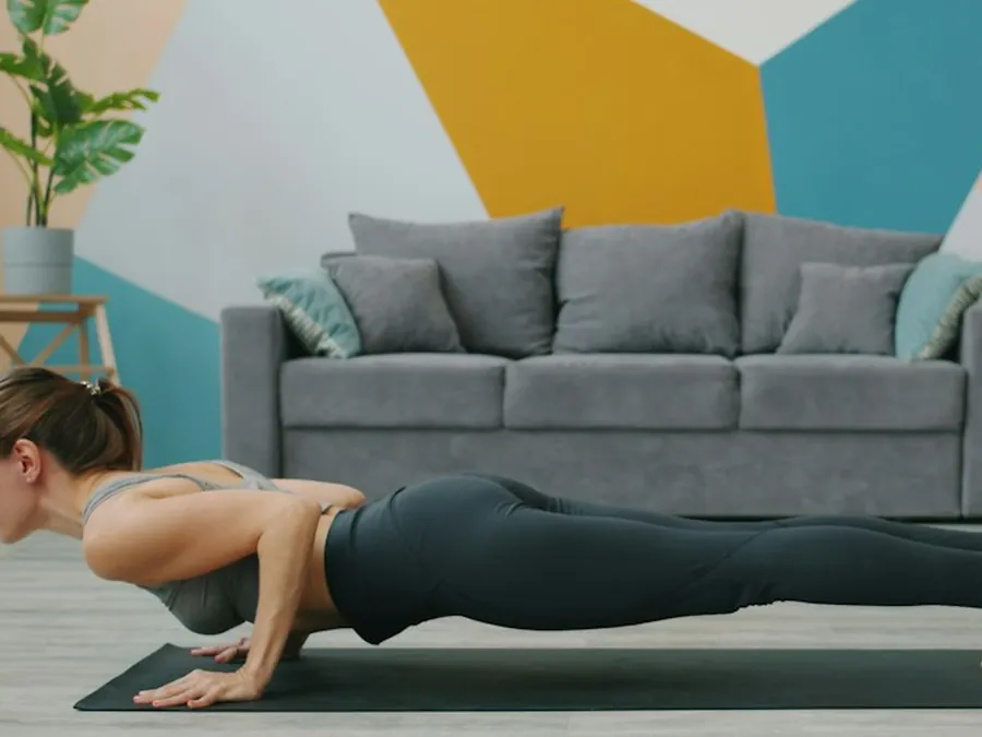 A woman doing a push-up on a yoga mat in her living room