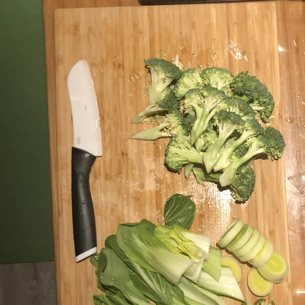 Broccoli, bok choy and leeks chopped on a wooden cutting board, from above