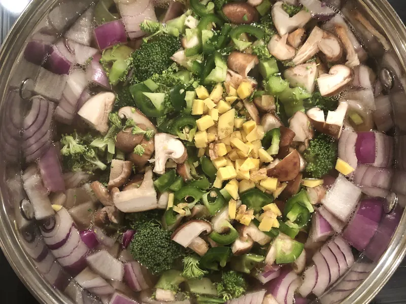 A large pot of chopped onion, broccoli, mushrooms, peppers and ginger, from above