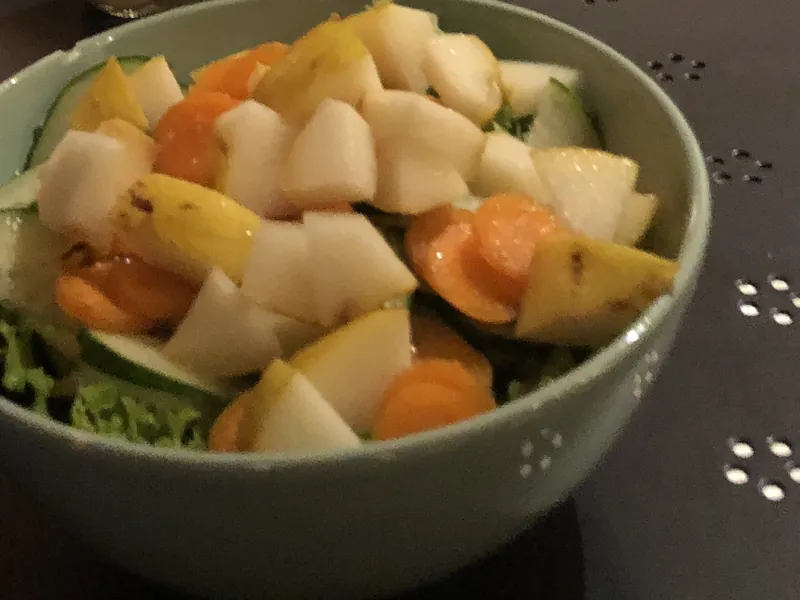 A bowl of salad with greens, cucumber, carrot and pear