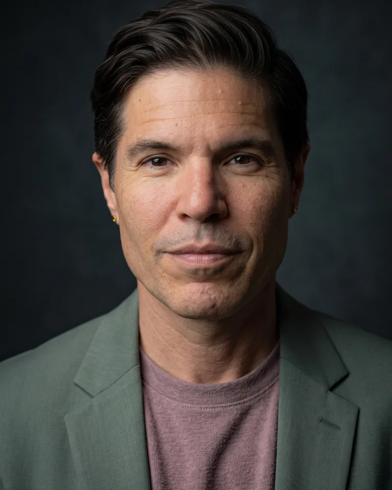 Headshot of JT Root in a sage-green blazer and mauve T-shirt.